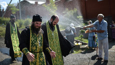 Мужчина поливает водой священнослужителей во время крестного хода Мужчина поливает водой священнослужителей во время крестного хода