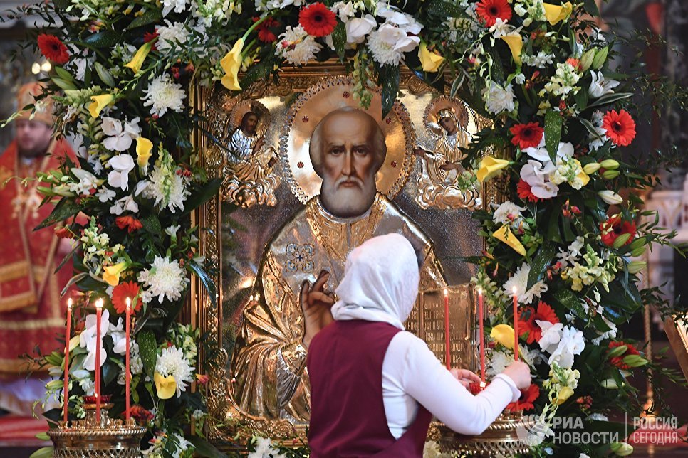 Женщина зажигает у свечи у иконы святителя Николая Чудотворца в храме Христа Спасителя, где находится ковчег с его мощами